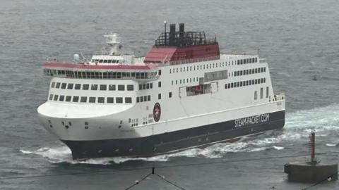 Manxman, a white ferry with navy on the base of the ferry, it is a large boxy ship on rough seas.