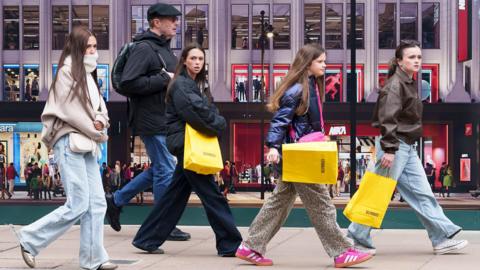 Shoppers on Oxford street walking from left to right of the photos carrying colourful bags 
