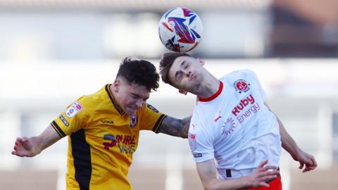 Jamie Miley of Newport County and Fleetwood Town's Mark Helm contest a high ball