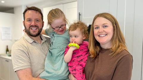 A family hug each other in the kitchen.