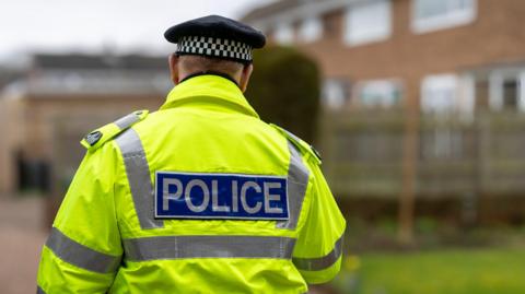 A police officer in a high-visibility jacket stood with their back to the camera on a street.