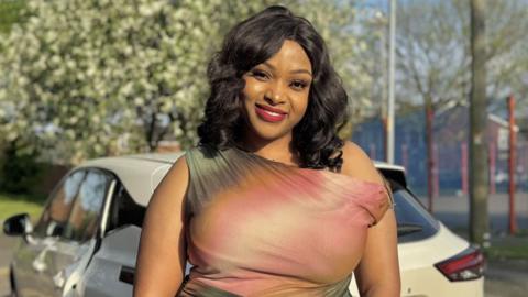 A woman smiling in front of a white car