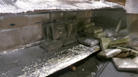 A silver heat insulator with clear bags of cannabis inside. It is on a grey floor. 