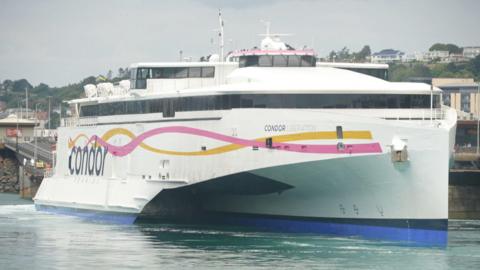 The Condor Liberation ferry, which has a white hulled-trimaran with a pink and yellow wave-like design along its side. 