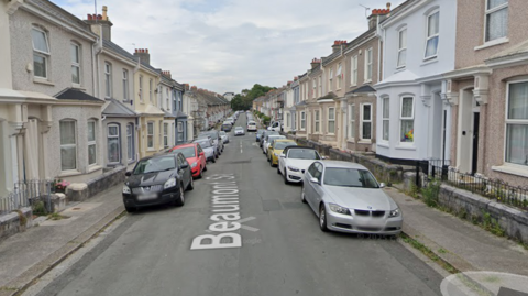 The image shows a residential street named Beaumont Street, lined with terraced houses on both sides. Several cars are parked along the street, and the houses share similar architectural styles with minor differences in colour and design.