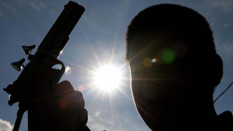 A silhouette of a young man holding a gun