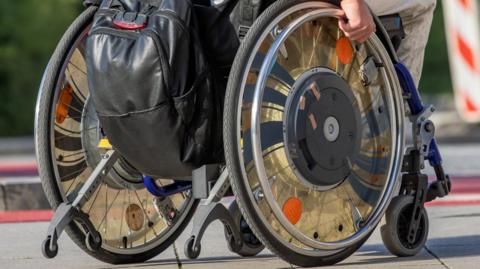 A generic image of a wheelchair. A man's hand is visible.