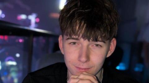 Elis Alan Ogilvy-Bardsley looking ahead in a portrait picture, with his chin resting on clasped hands.