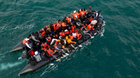 An aerial photo of a small boat overloaded with people in life jackets.