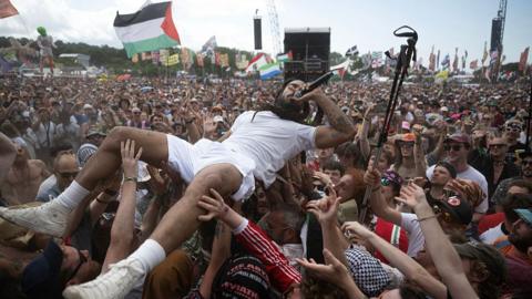 Bobby Vylan, of British duo Bob Vylan, is pictured on his back crowd-surfing. He is holding a microphone to his mouth.