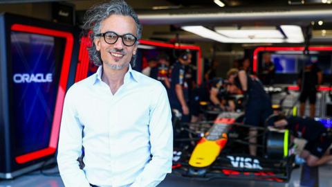 Laurent Mekies stands in front of the Red Bull garage as mechanics work on a car