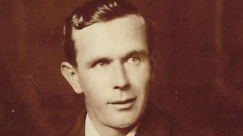Black and white photo of Mr Barker. He is looking to the right side of the camera and has dark, slicked back hair. 