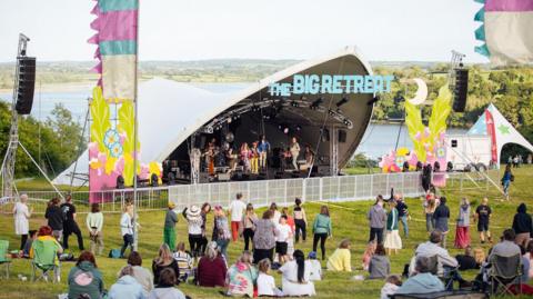 The Big Retreat festival, showing a performance on a stage with people dancing and sitting in a field watching