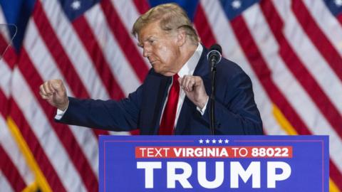 Donald Trump seen dancing at a lectern in Virginia, with several US flags in the background