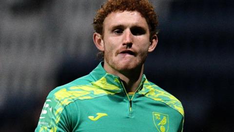 Norwich City striker Josh Sargent, wearing a green and yellow tracksuit, leaving the pitch during a pre-match warm-up session