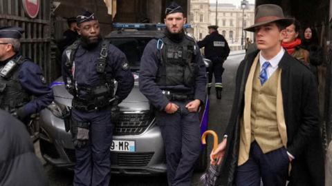 A well-dressed Pedro Elias Garzon Delroux walking past police officers as they block access to the Louvre museum.