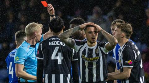 Oliver Norburn with his hands on his head as he walks away from his team-mates and referee after he is shown a red card.