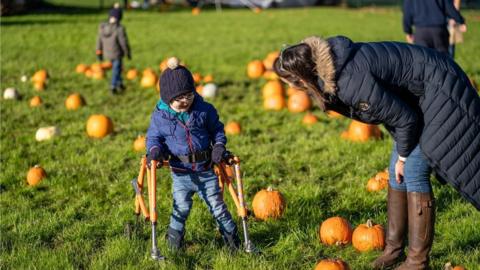 A boy using a walking frame laughs with a woman in the pumpkin patch