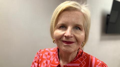 Image of Donna. She has blonde hair and is wearing pink/red dress.