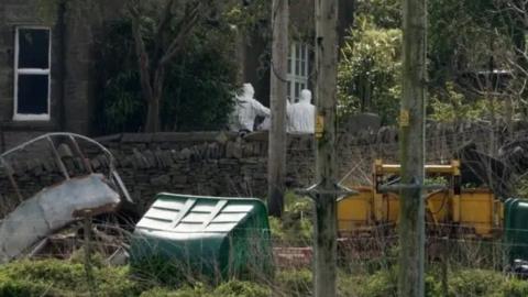 Police in white suits viewed on the farm from afar