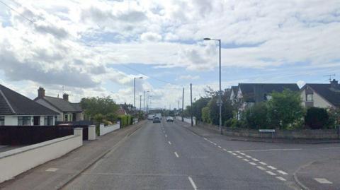 A Google Street View image of a residential road. There are two cars in the distances and a number of homes on either side of the street. 