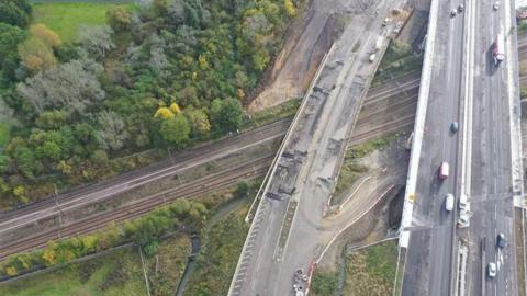 The picture shows an aerial image of an old bridge, no longer in use with a new one next to it. Both cross a railway line  