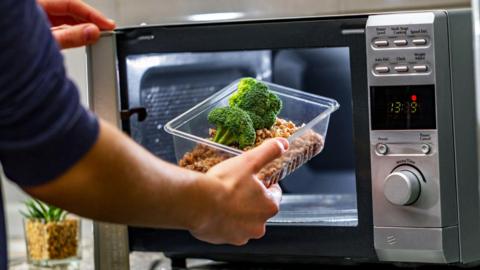 A man putting a plastic container with leftover food into a microwave.
© Getty Images