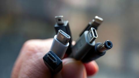 Close-up of a man's hand holding a bunch of cables with different connectors.