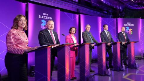 The six party leaders standing at lecterns on the purple studio set with BBC election branding behind them.
