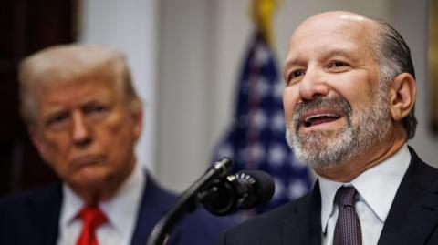 US Commerce Secretary Howard Lutnick wears dark suit, patterned tie and white shirt as he speaks at the White House, on 3 March 2025. President Donald Trump is standing to Lutnick's right. 