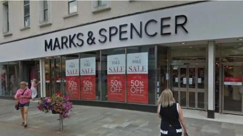 Shoppers go in and out of Marks & Spencer store in Blackburn. Its windows are emblazoned with red "up to 50% off" sale signs.