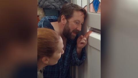 A man and woman talk through the letterbox