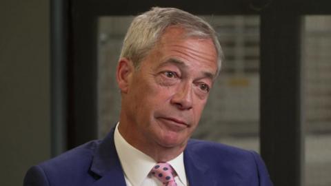 Nigel Farage being interviewed in a blue suit and pink spotted tie