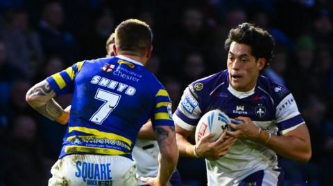 Wakefield's Isaiah Vagana, wearing a white and blue shirt, runs at Warrington's Marc Sneyd