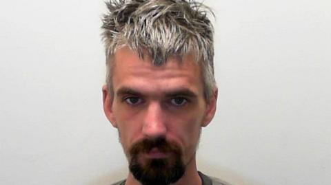A police mugshot of Sean Beard. He has a dark goatee beard and messy gray hair.