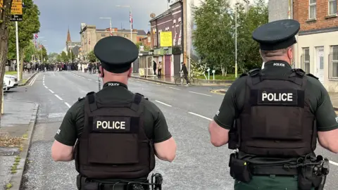 Police in Belfast stand watching a gathering of people