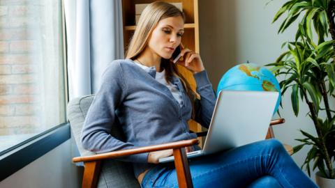 Young woman sitting in arm chair using laptop, with a globe behind her