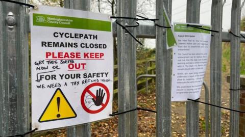 A laminated sign warning people that a cycle path is closed, telling people to 'PLEASE KEEP OUT'.