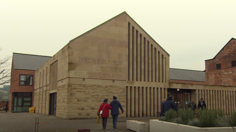 Large stone building with triangular roof, people walking inside