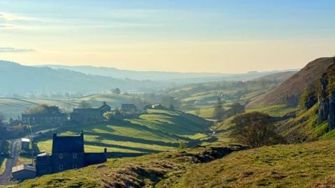 Rolling hills and fields bathed in sunshine with yellow and blue sky overhead