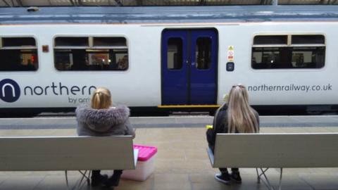 women sit on platform looking at northern railway train