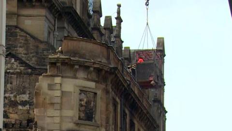 Crane lowers debris container beside damaged historic building as demolition gets under way.