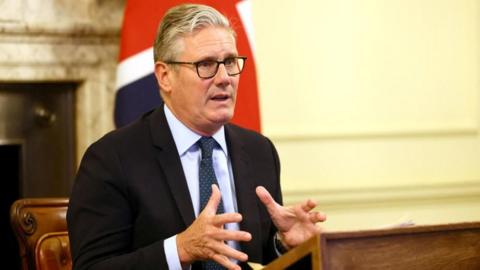 Starmer wears a suit and glasses and speaks at the cabinet table.