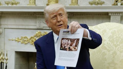 U.S. President Donald Trump holds up a printed article from "American Thinker" while accusing South Africa President Cyril Ramaphosa of state-sanctioned violence against white farmers in South Africa 