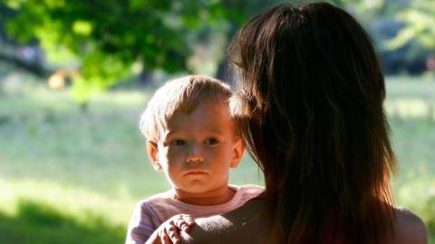 A little boy looking over a woman's shoulder