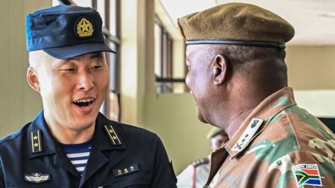 A naval officer from China and South Africa military officer - both in their respective uniforms - greet each other.