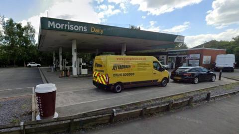 Street view of Morrisons Daily in Totnes with a yellow van and black car at the filling station
