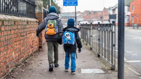 Two boys with backpacks pictured from the back walking forward on a pavement