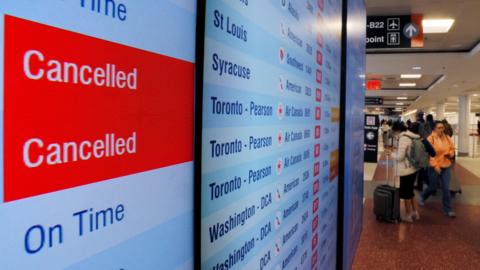 A board shows two cancelled American Airlines flights and three on time, as airlines cancelled