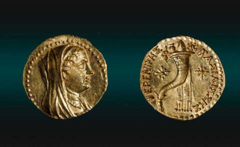 One side of the gold coin showing Queen Berenice wearing a tiara, a veil, and a necklace. The other side shows two stars and a cornucopia, also known as the "horn of plenty' - typically shown as a curved, horn-shaped basket overflowing with fruits, vegetables, and flowers.